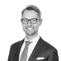 Black and white portrait of a smiling man wearing glasses, a suit, and a tie, with a professional and confident appearance.