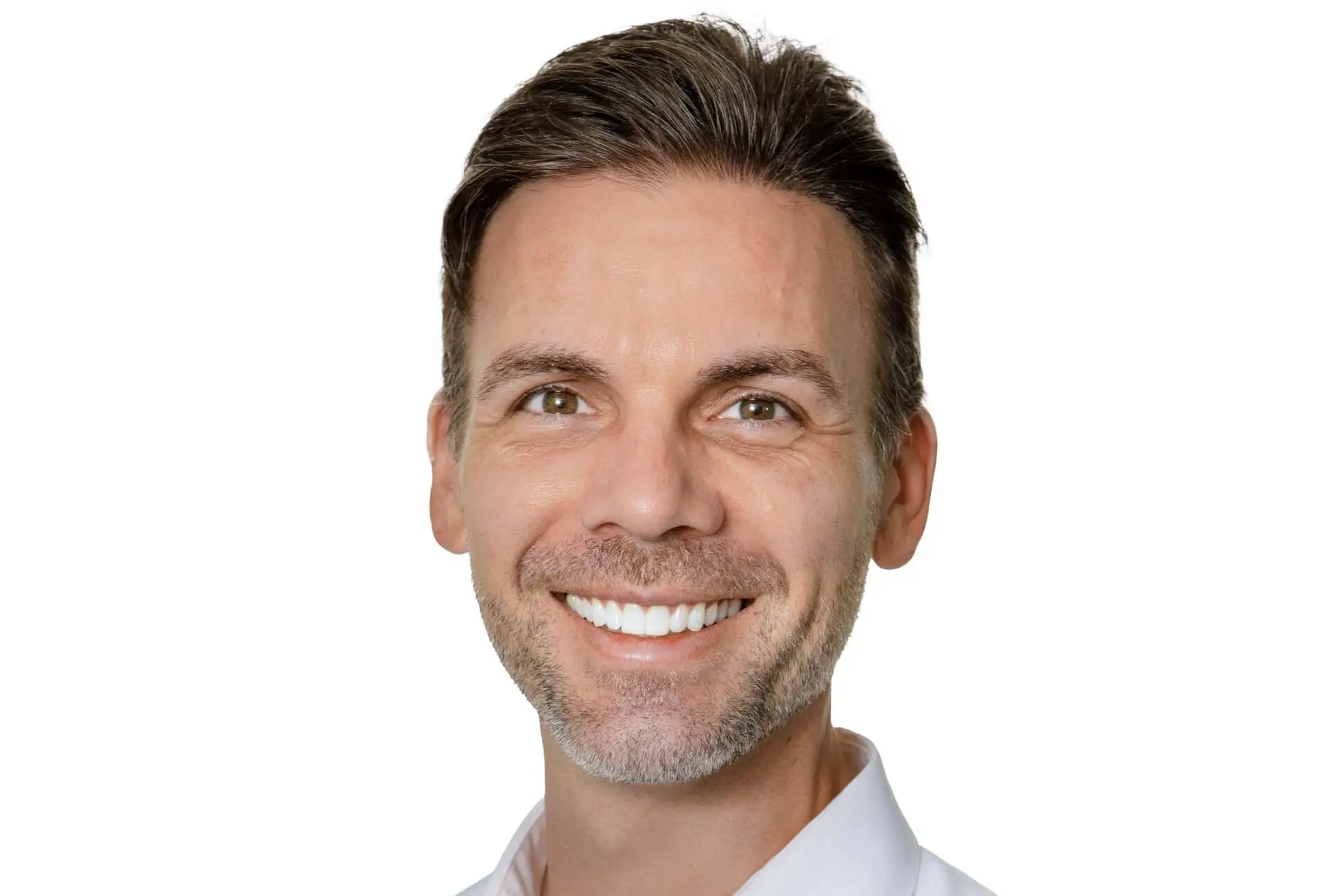 Smiling man with short dark hair and light stubble, wearing a white shirt, against a plain background.