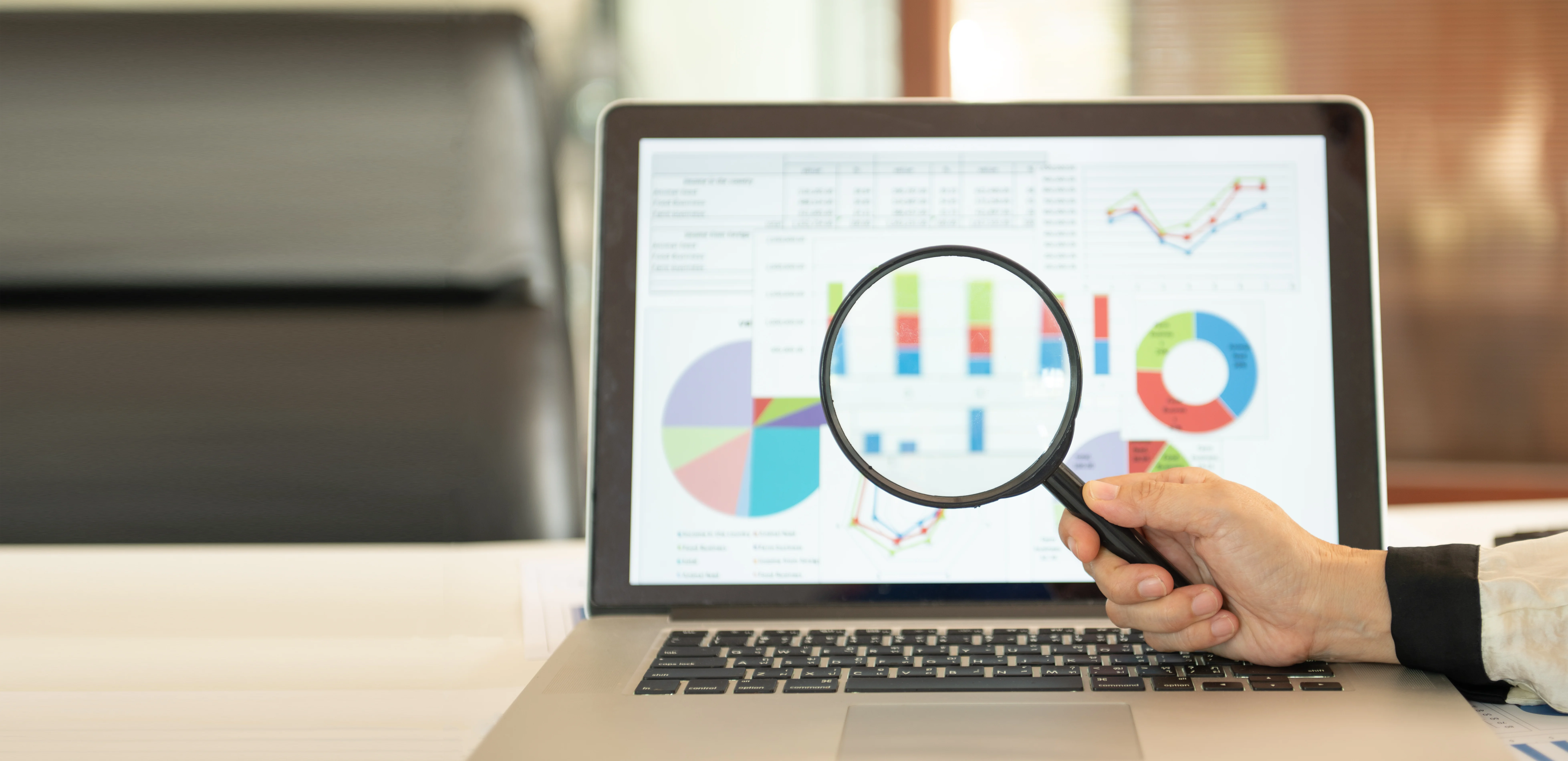 Magnifying glass on laptop monitor with statistics.